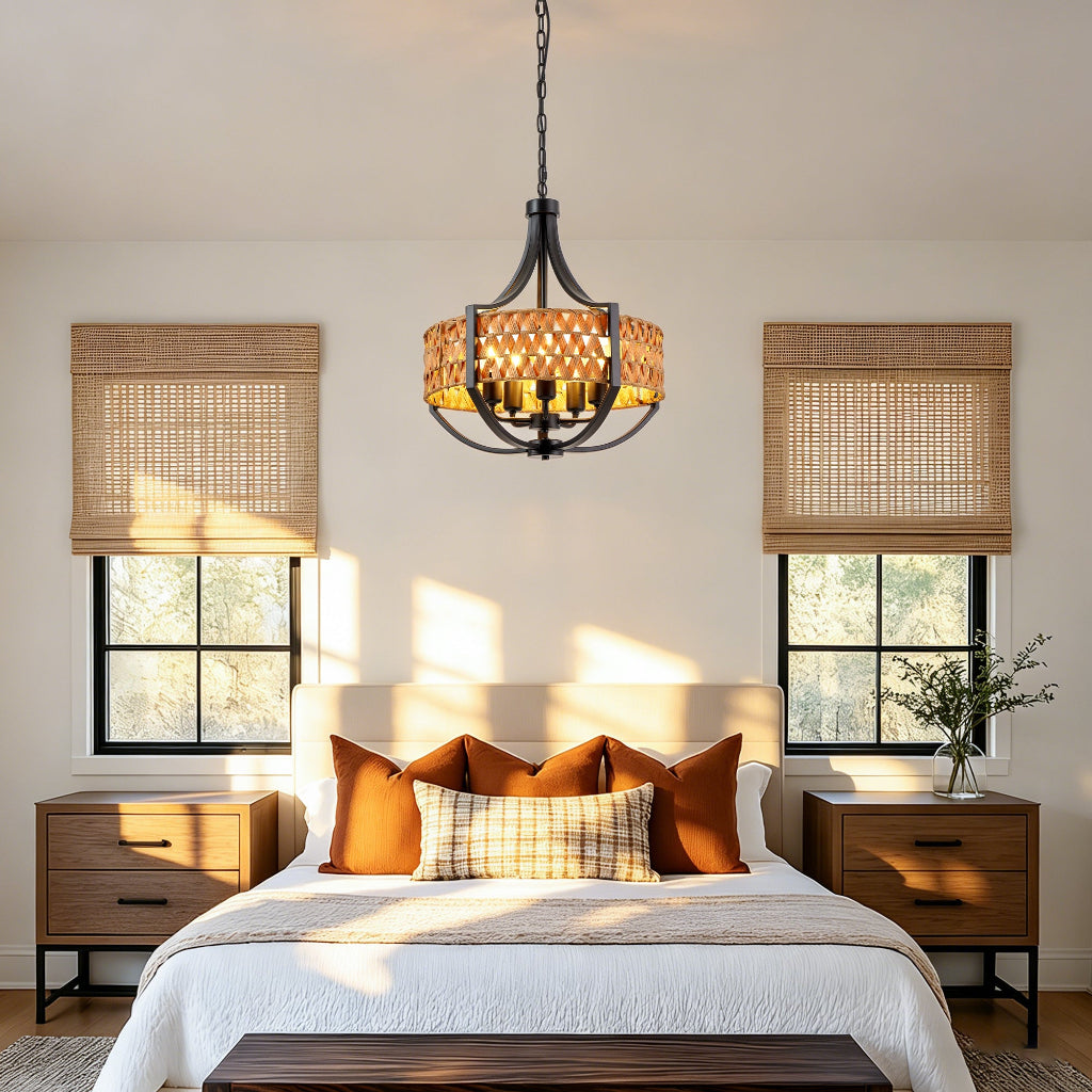 A hanging pendant chandelier with a black metal frame and a warm amber woven shade is centered above a neatly made bed in a bright, sunlit bedroom. Two matching wood nightstands, woven window blinds, and a bed with orange and plaid pillows are visible.