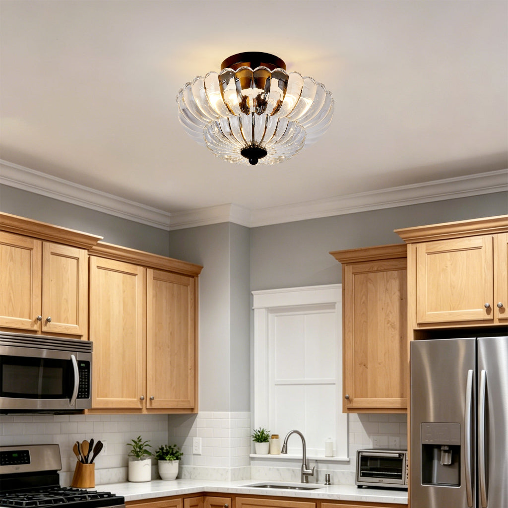 A modern semi-flush mount ceiling light with a scalloped clear glass shade and a dark brass-toned top and bottom cap, installed in a kitchen ceiling.