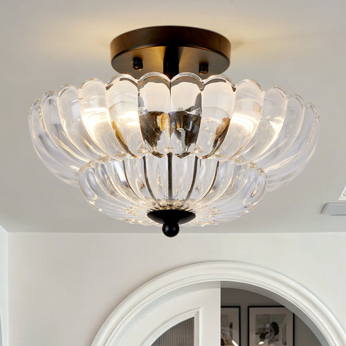 A semi-flush mount ceiling light fixture with a clear glass petal-shaped shade and a dark bronze metal canopy, shown illuminated in a home interior setting.