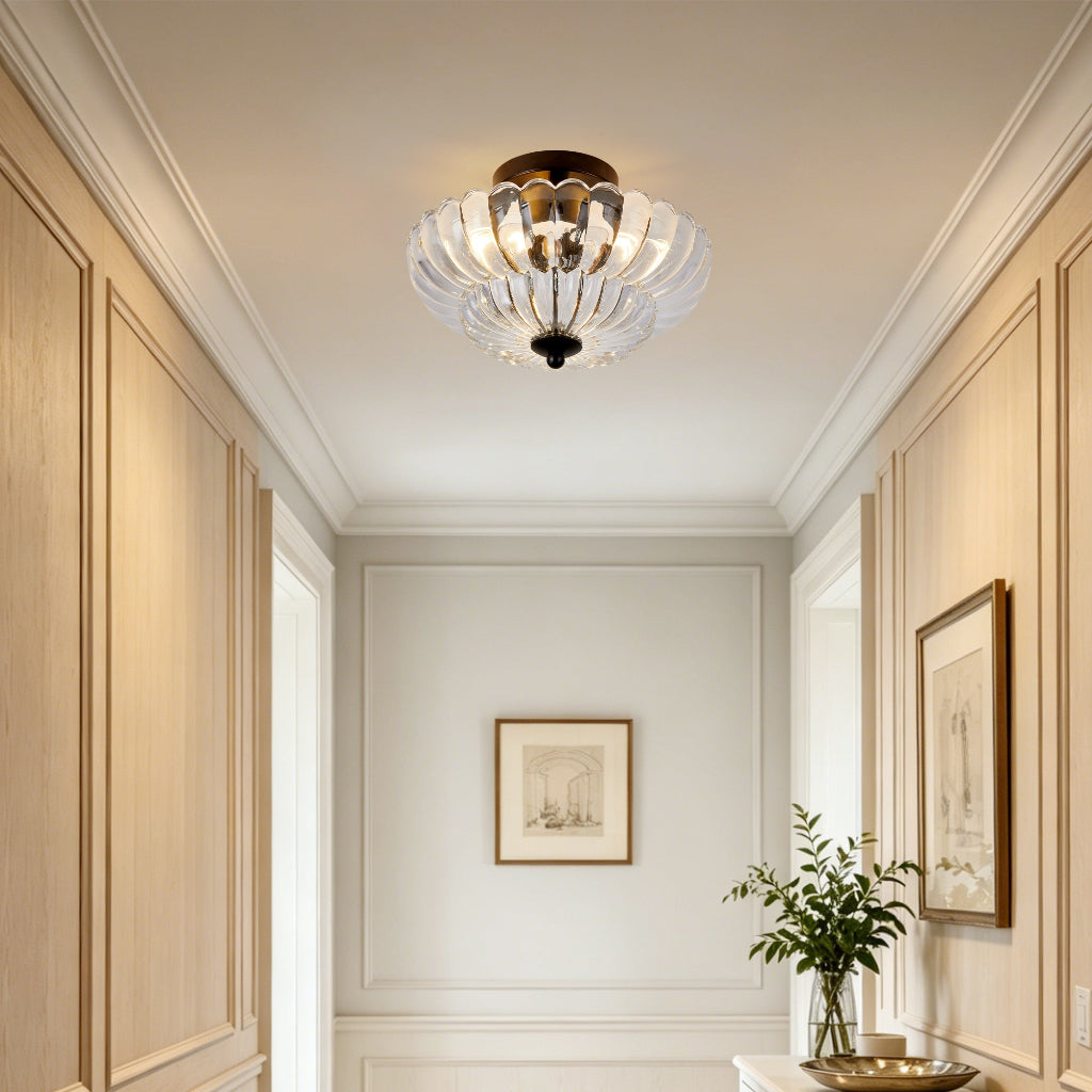 A modern semi-flush mount ceiling light fixture with clear glass petal-like shades and a dark bronze metal frame, installed in a bright hallway with beige wood paneling.