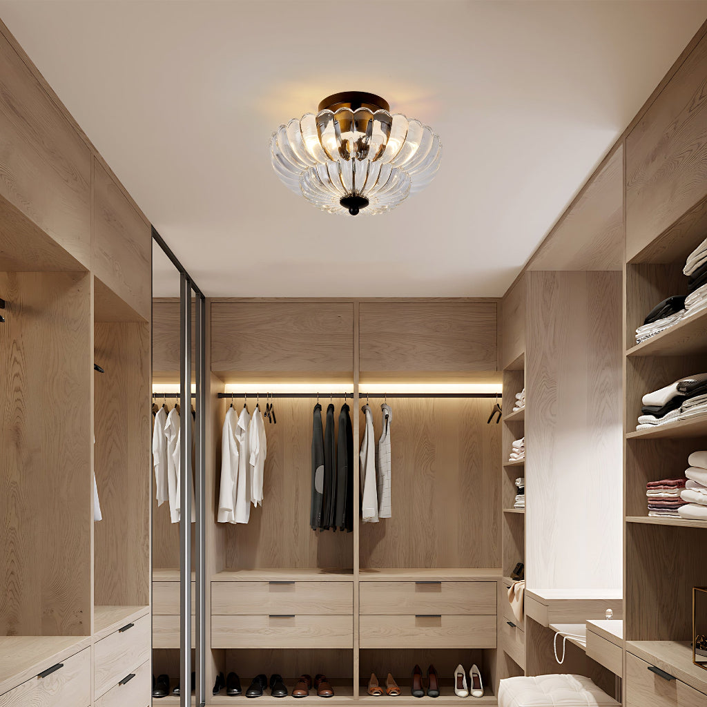 A modern glass chandelier with a warm brass fixture hangs in a well-lit, contemporary walk-in closet with light wood cabinetry and clothing racks.